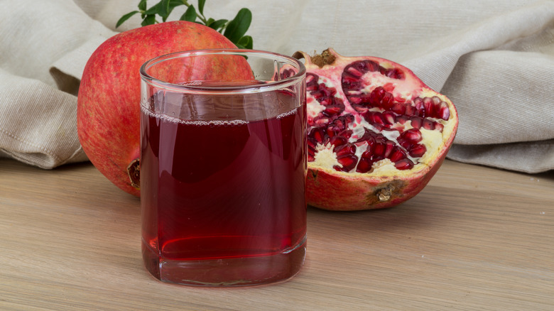 Pomegranate juice glass in with fresh pomegranates and a beige cloth in the back