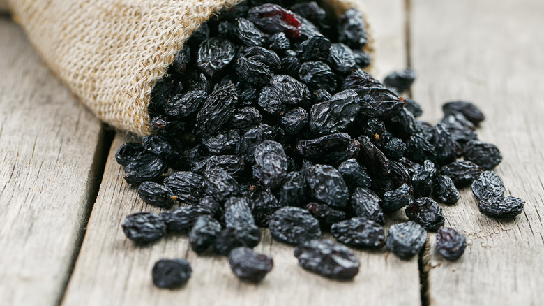 Black raisins spilling out of a burlap sack on a wooden table