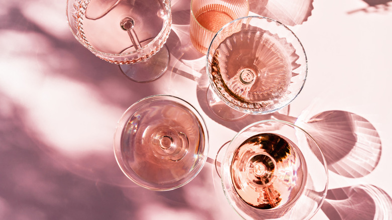 Top view of various types of glasses filled with rose wine on a pink table