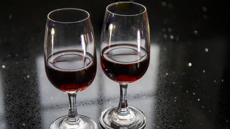 Two glasses of ruby red port wine on a black counter