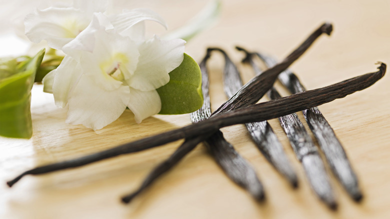 Close-up of two vanilla beans crossed on top of four vanilla beans next to a white vanilla flower