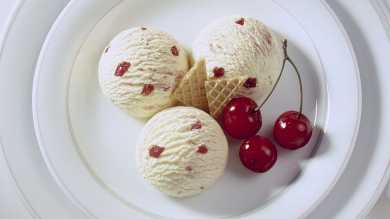 Three scoops of cherry vanilla ice cream on white platter with fresh cherries