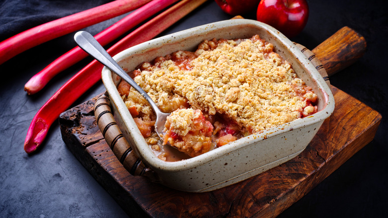 Rhubarb crumble with stalks and spoon on wooden board