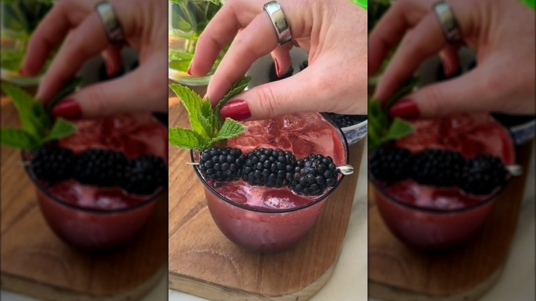 Placing mint sprig into a blackberry spritz cocktail