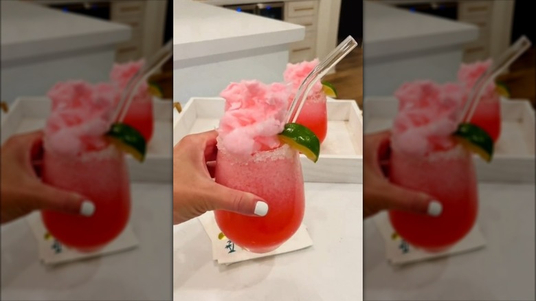 Hand holding cotton candy margarita with a straw and lime wedge