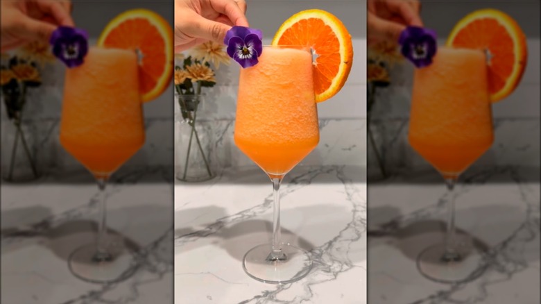 Frozen Aperol spritz cocktail in a glass with orange slice and flower garnish