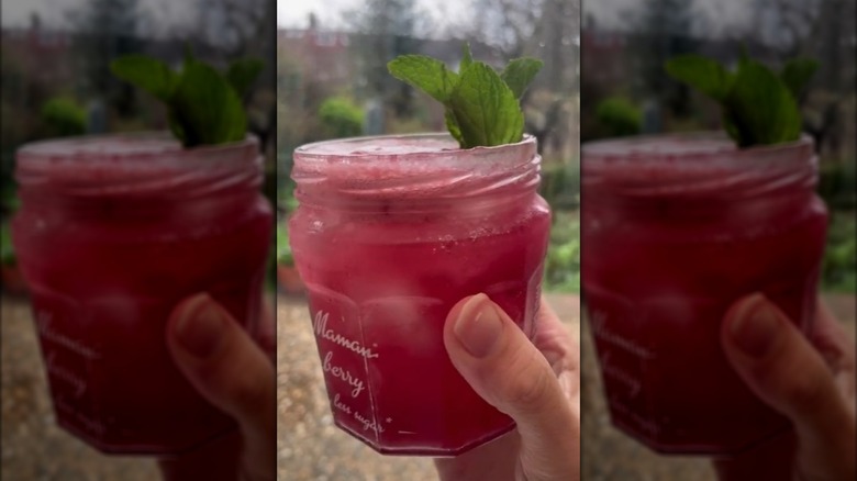 Hand holding jam jar cocktail with mint sprigs