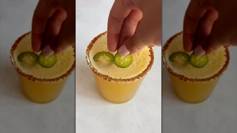 Placing sliced jalapeños on top of a spicy margarita cocktail