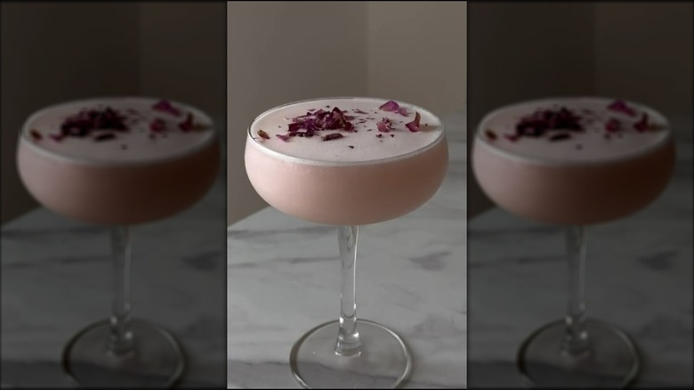 Pink gin sour cocktail in a glass with rose petals