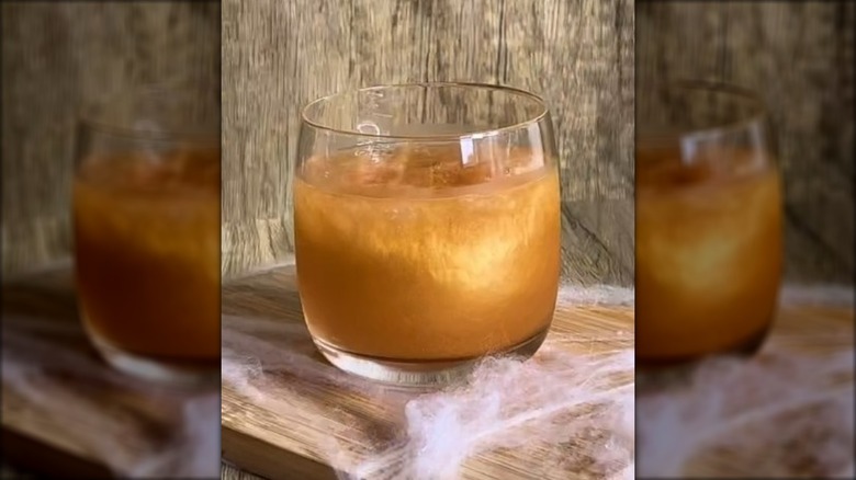 A glass of a poison apple cocktail on a wooden board with faux spider webs