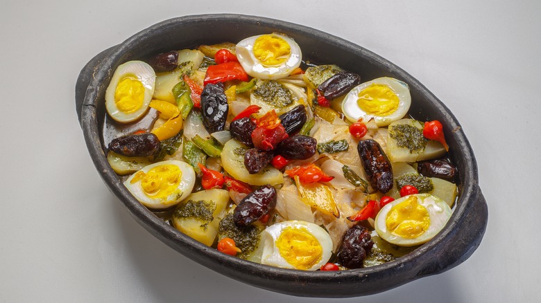 Hard-boiled eggs, fish, and olives in black pan