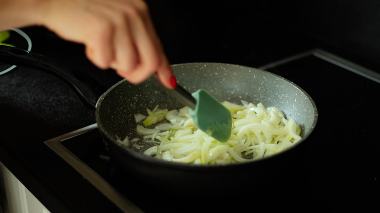 Person sauteing onions in frying pan