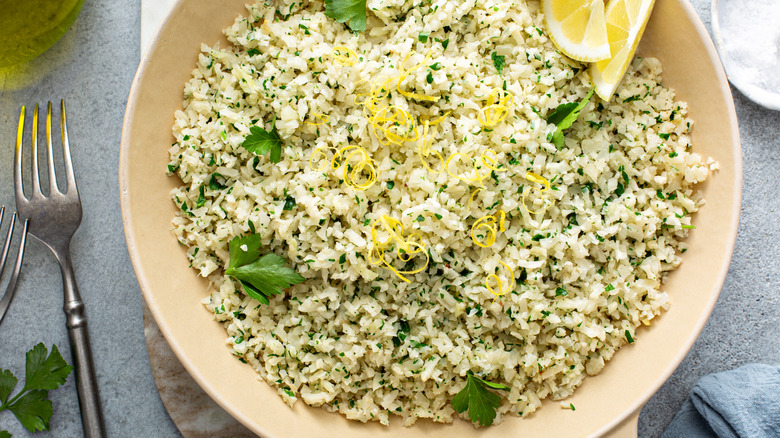 Cauliflower rice in white pan with lemon zest and parsley