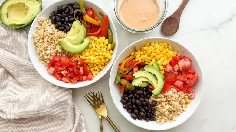 Cauliflower rice burrito bowls topped with corn, peppers, black beans, tomatoes, and avocado