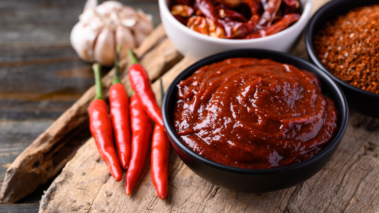 Bowl of gochujang on a wooden plank next to chili peppers