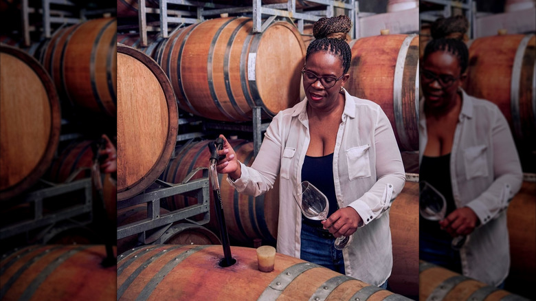 producer winemaker Ntsiki Biyela testing wine from barrel in a wine cellar surrounded by wooden barrels