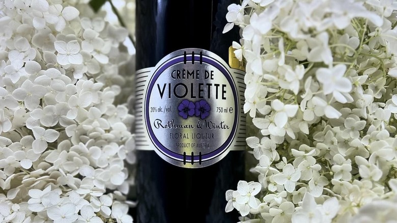 Bottle of creme de violette resting on flowers