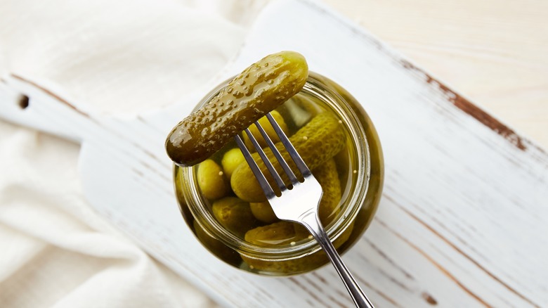 a pickle on a fork above a pickle jar