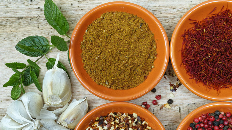 Bowl of ras el hanout in red ceramic dish surrounded by other spices