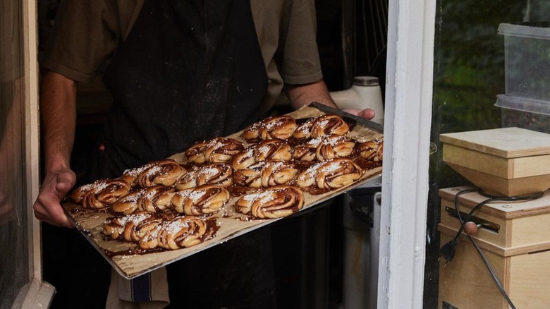 person holding tray of kanelbullar with pärlsocker