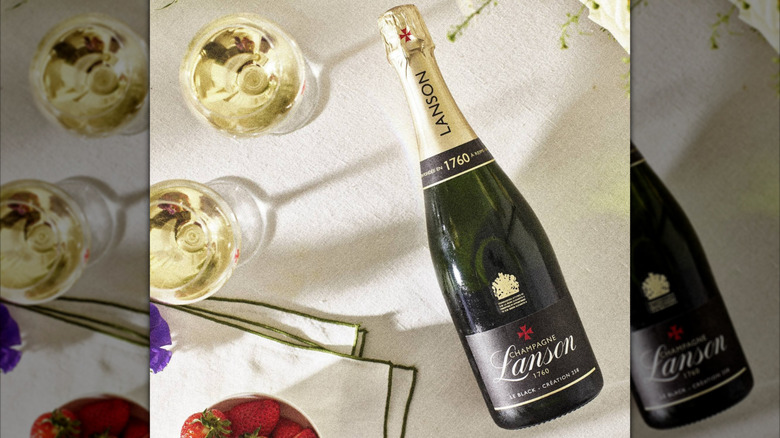 champagne bottle on surface with glasses and strawberries