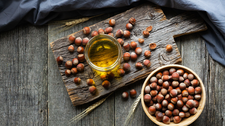 Hazelnut oil in glass bowl surrounded by whole hazelnuts on a wooden surface