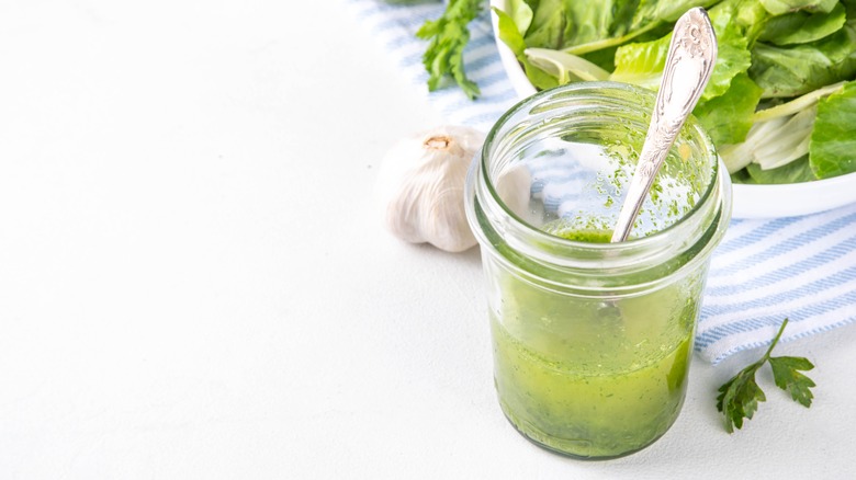 Herb oil in mason jar next to bowl of salad greens