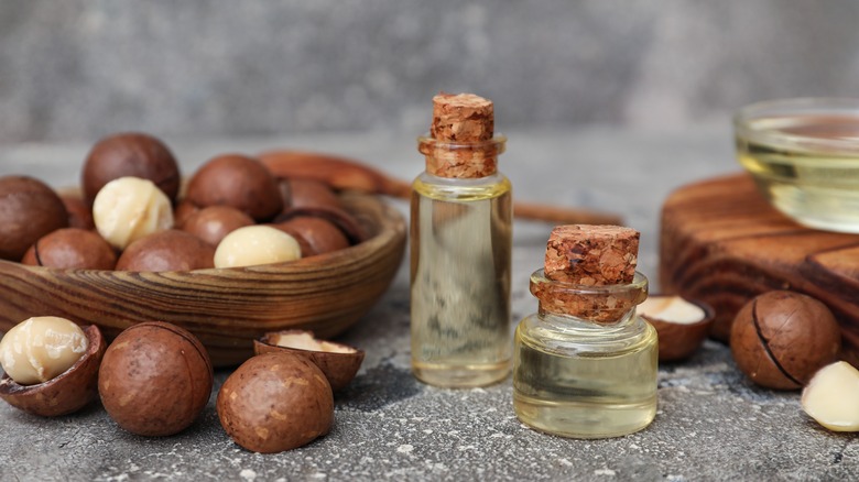 Vials of macadamia nut oil next to wooden bowls of macadamia nuts