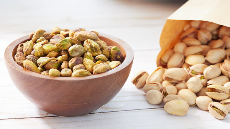 Pistachios in a dish next to a paper bag full of pistachios