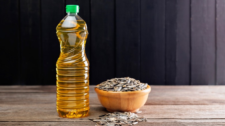 Oil bottle next to a bowl of sunflower seeds on a wooden table