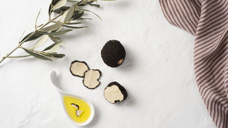 Truffles sliced up on white table surface next to spoonful of truffle oil