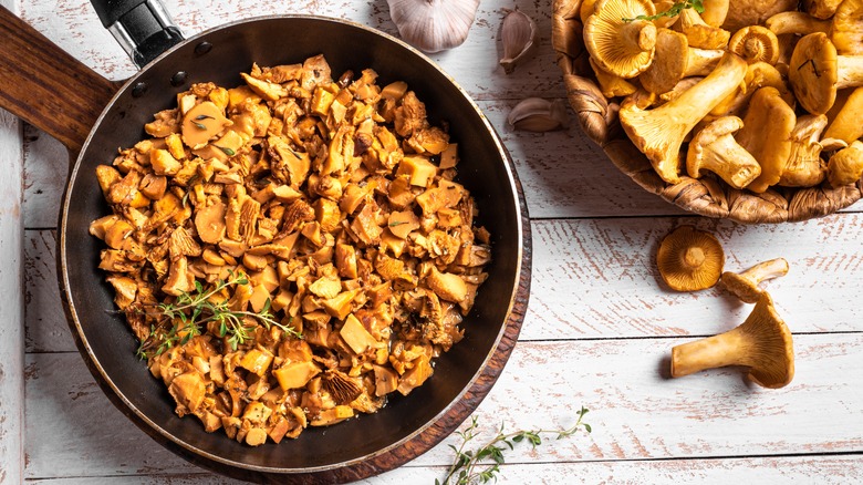 Fried chanterelle mushrooms in pan with fresh mushrooms in bowl