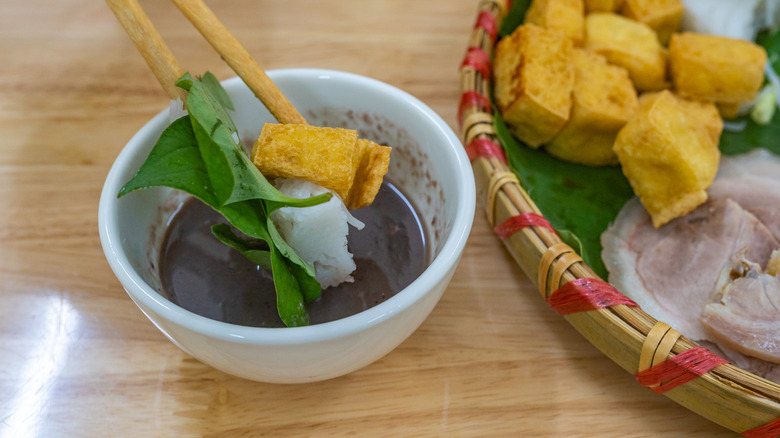 person dipping tofu into shrimp sauce