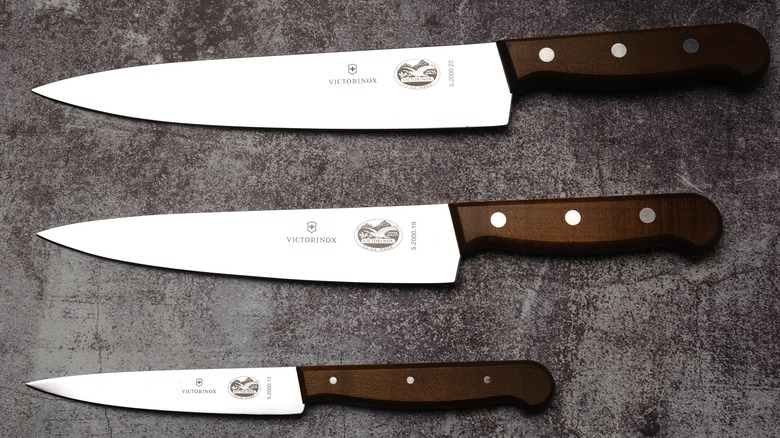 Three Victorinox kitchen knives with wooden handles on a rustic surface