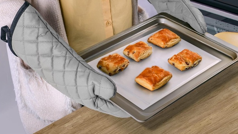 Person wearing oven mitts holding a tray with five pastries on it