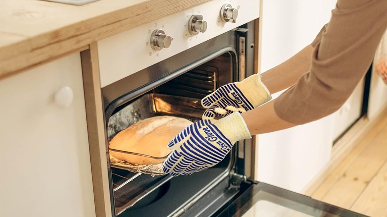 Person wearing oven gloves holding a hot dish in opened oven