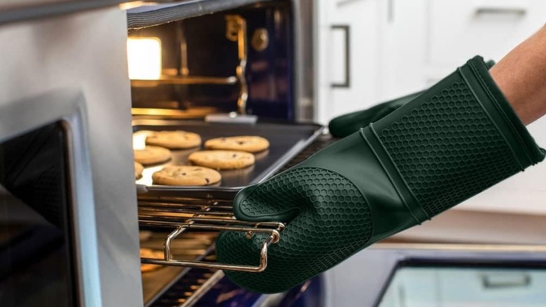 Person wearing oven mitts pulling out rack of baked cookies from oven