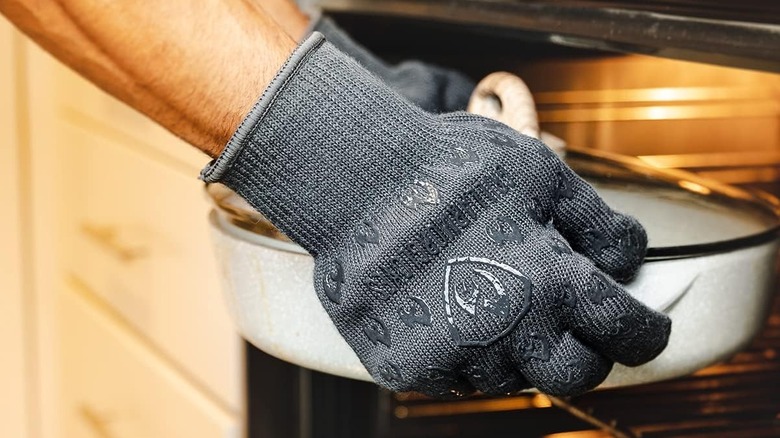 Person wearing oven gloves grabbing onto casserole dish in front of oven