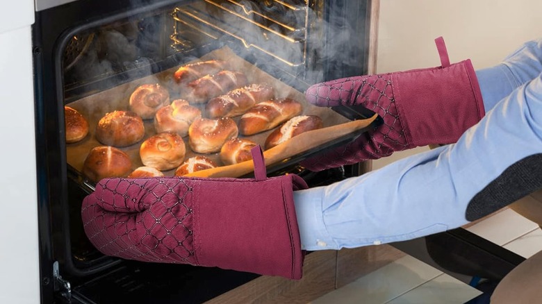 Person wearing IXO oven mitts removing sheet pan of baked breads from oven