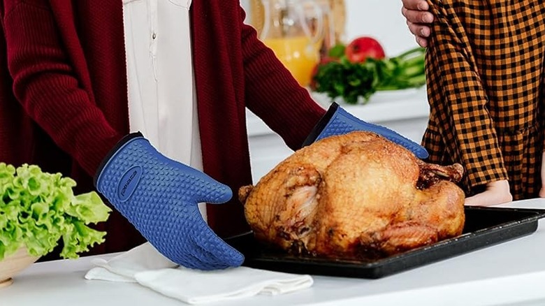 Person wearing Kitchen Perfection oven gloves extending arms toward cooked turkey on pan