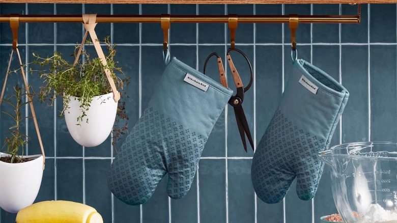 Pair of oven mitts hanging onto hooks in front of kitchen wall tiles