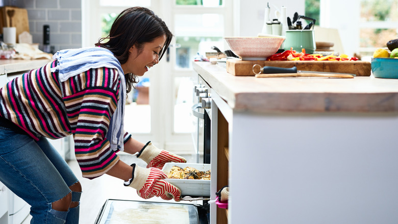 Person using oven gloves while handling a dish of food in front of oven