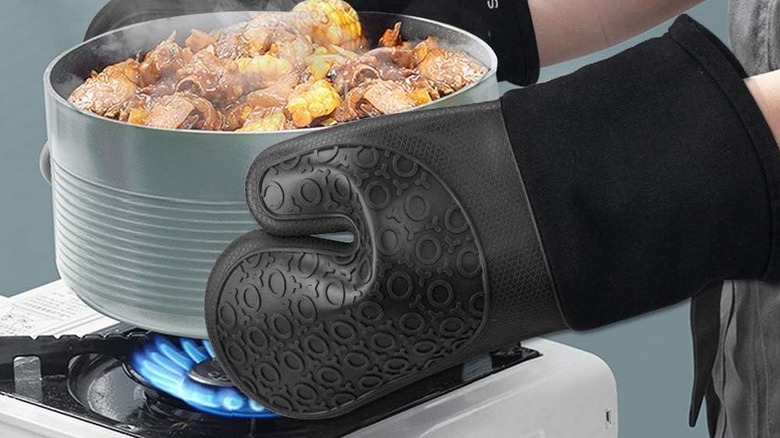 Person wearing oven mitts holding pot of hot food over stove