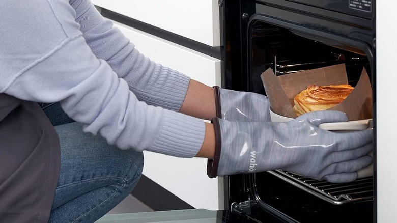 Person wearing Wahoo gloves holding a pot with food in oven