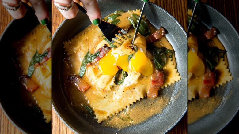 person cutting a large ravioli with egg yolk in a bowl