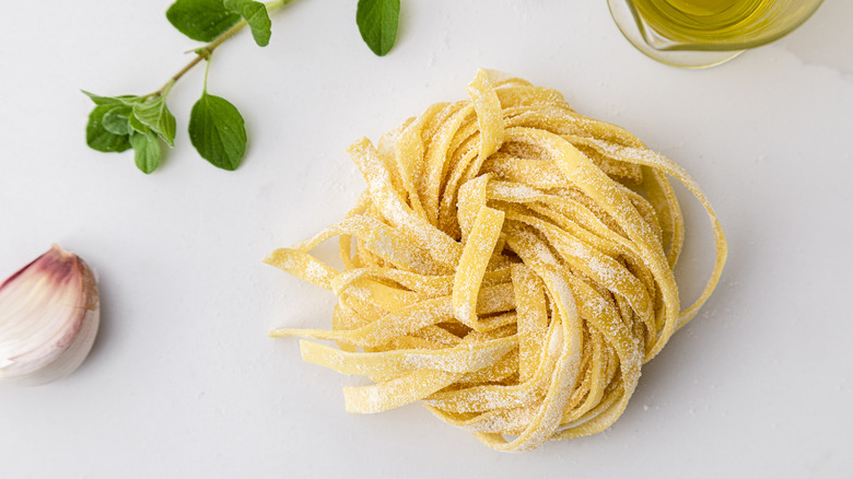 Raw pasta ball on white background next to oregano and garlic