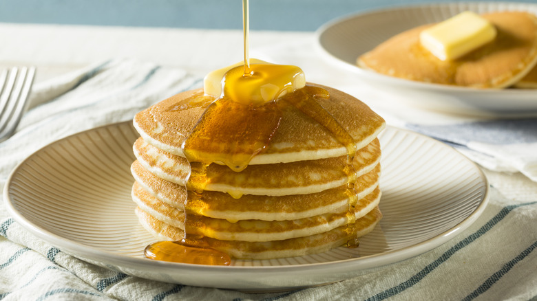 Syrup being poured on a stack of pancakes