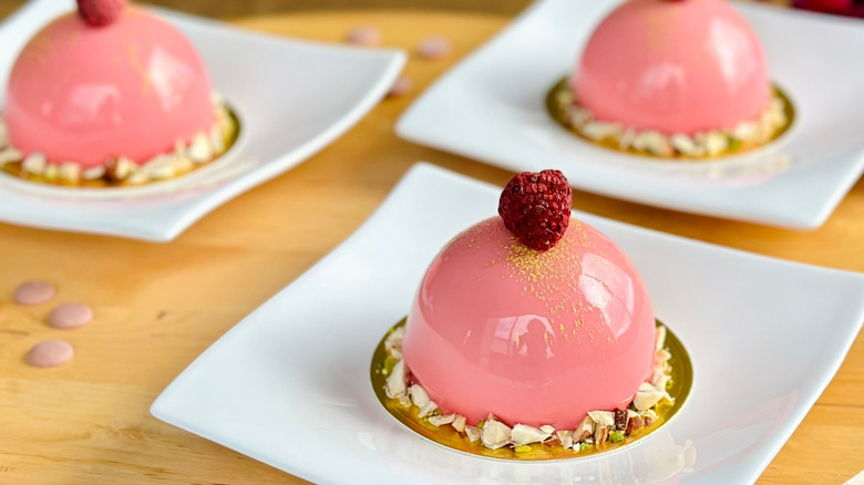 Small pink mousse cakes with a mirror glaze on white plates