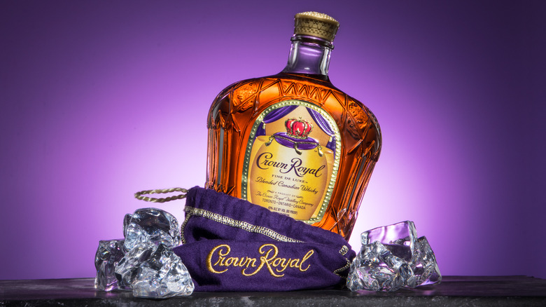 Bottle of Crown Royal with bag and ice on purple background