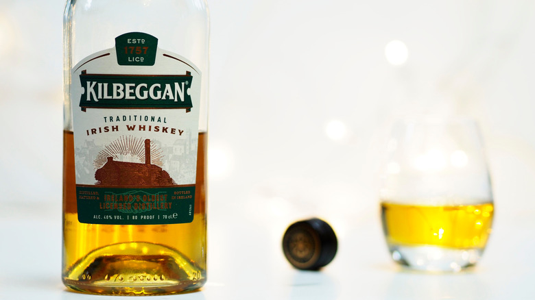 Partially empty bottle of Kilbeggan with glass on white background